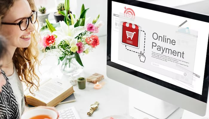 A woman smiling while looking at a computer screen displaying an online payment interface with a shopping cart icon.